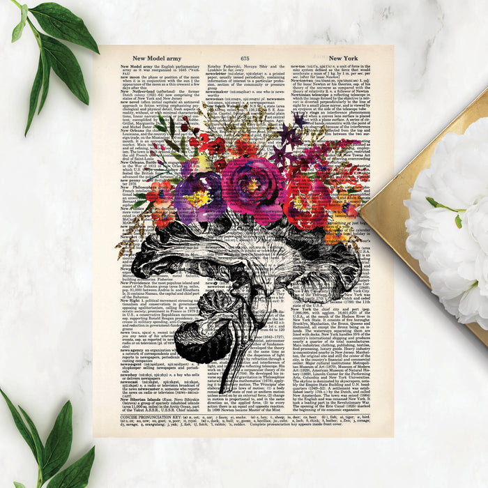 vintage etching of the cross section of an anatomical brain accented with watercolor tropical flowers in shades of pinks, purples, yellows, and golden tones printed on a dictionary page