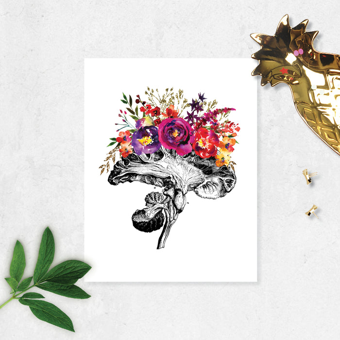 vintage etching of the cross section of an anatomical brain accented with watercolor flowers in shades of pinks, purples, and golden tones on matte white paper