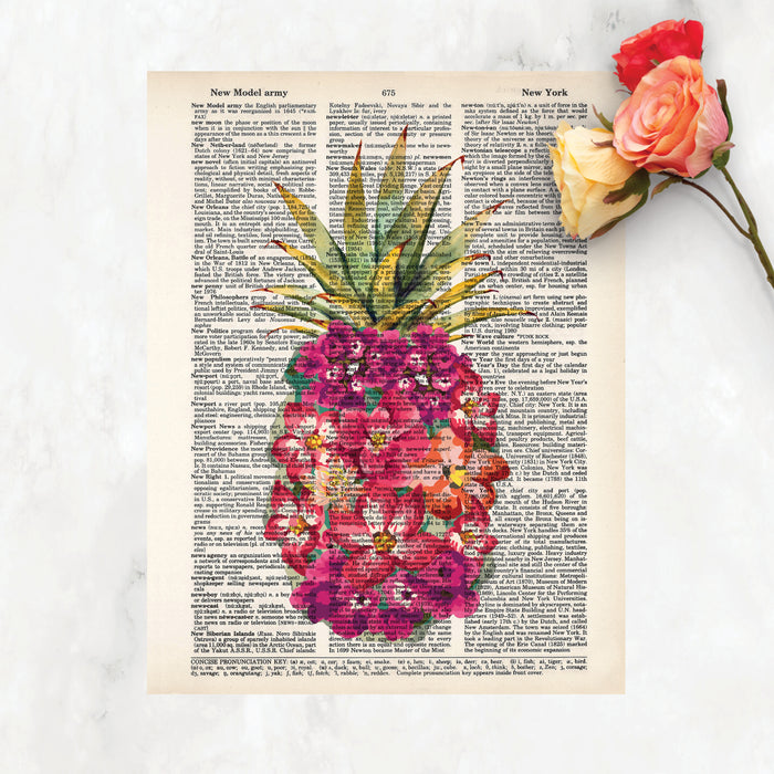 shades of pink watercolor tropical flowers form the shape of a pineapple with traditional pineapple greenery at the top printed on a dictionary page