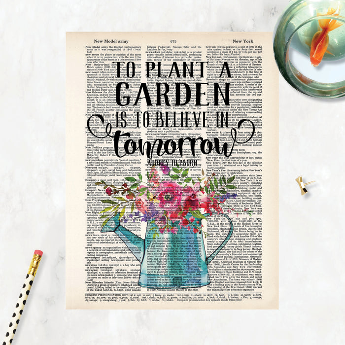 to plant a garden is to believe in tomorrow quote from Audrey Hepburn above a blue watering can filled with pink and purple flowers with greenery printed on a dictionary page