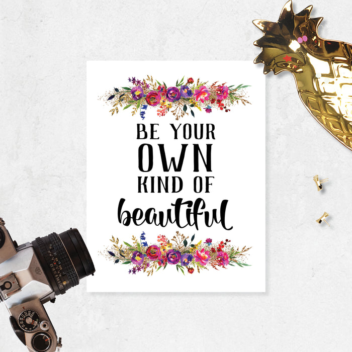 be your own kind of beautiful quote with watercolor flowers at the top and bottom of matte white paper. Flowers are pinks, purples, yellow, and golden tones