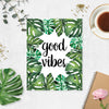 good vibes in black ink surrounded by tropical monstera leaves on matte white paper