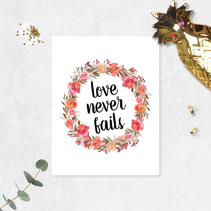 love never fails surrounded by a wreath of pink and coral watercolor flowers with greenery printed on matte white paper