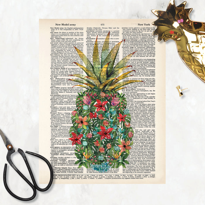 watercolor monstera leaves along with pink, red, peach, and blue flowers along with red and blue shells and coral form a pineapple shape with a traditional pineapple top printed on a dictionary page